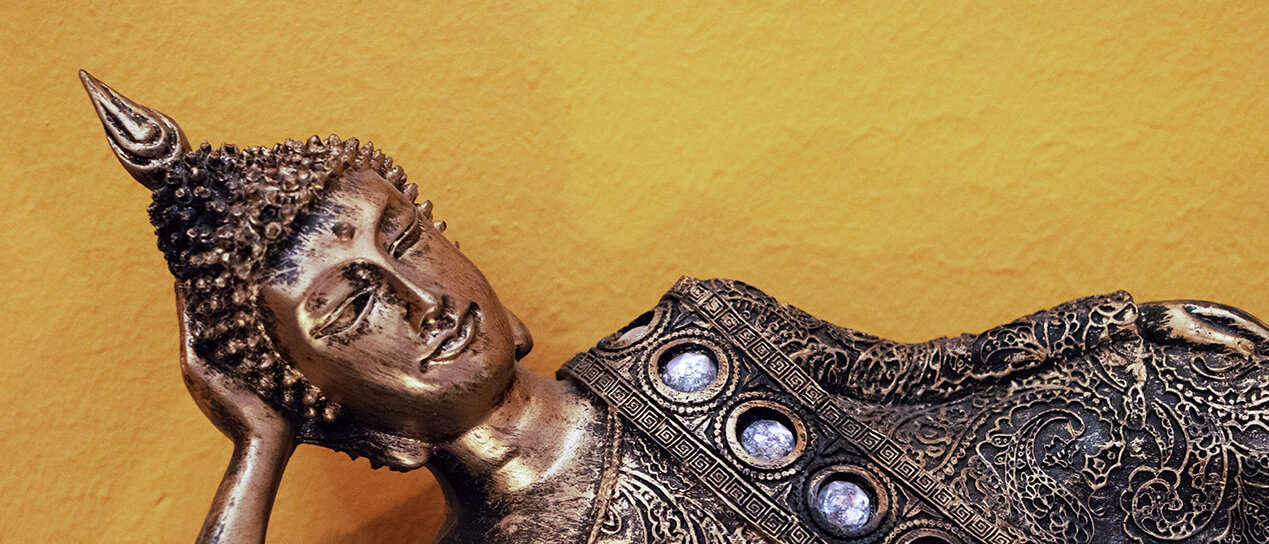 Busch: Buddhafigur liegend mit Kerzen im Vordergrund