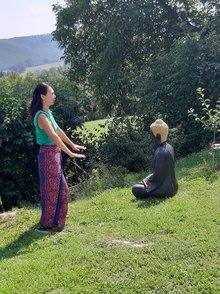 Qi Gong im Garten Eine Frau macht Qi Gong in einem grünen Garten neben einer Buddha Statue