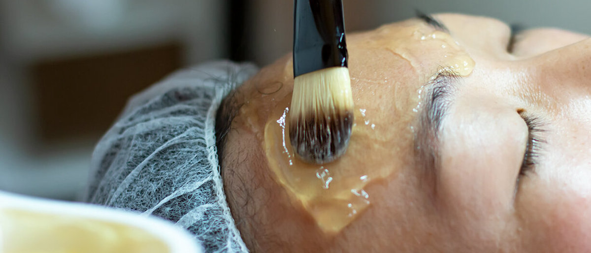 Kosmetikbehandlung Patientin mit Schutzhaube für Haare bekommt Gel mit Pinsel ins Gesicht aufgetragen