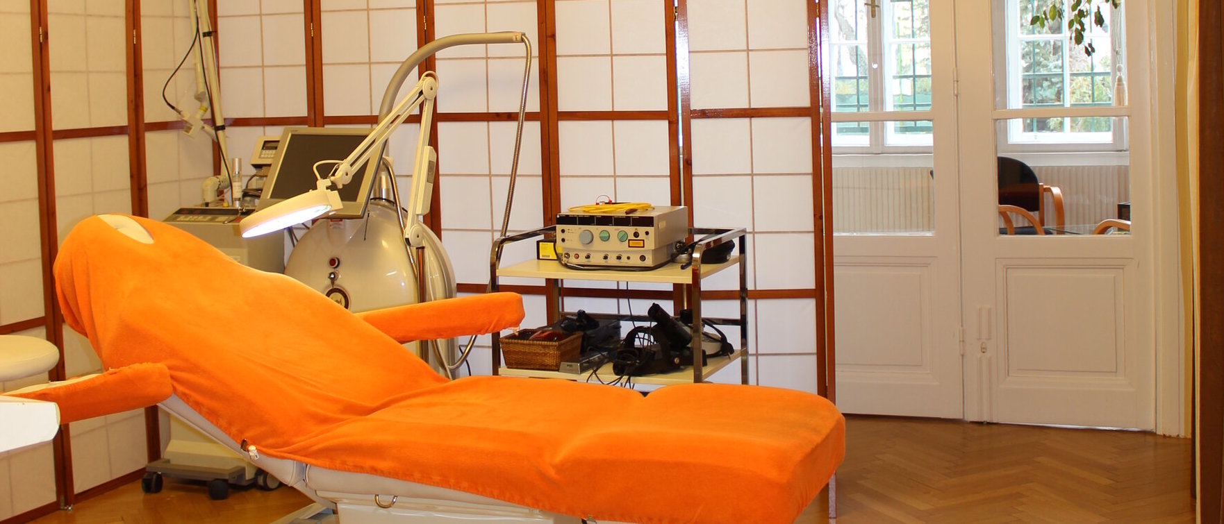 David Hume Orange Behandlungsliege in einem Raum mit Paravents und Lasergeräte im Hintergrund